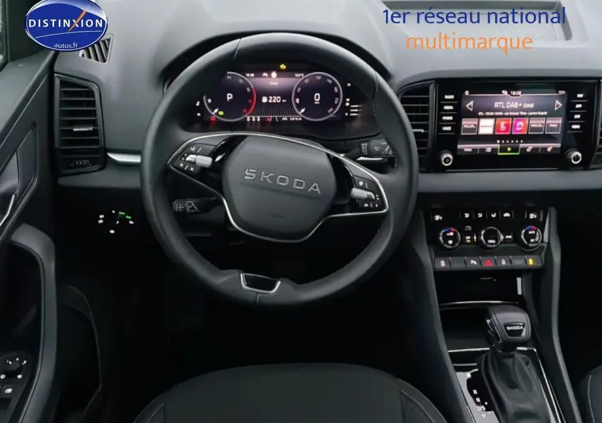 Vue intérieure avant du Skoda Karoq blanc glacial 2025, volant multifonction et écran tactile central visibles.