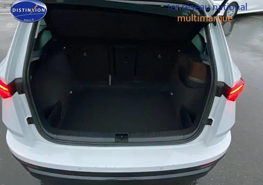 Coffre ouvert vu de l'arrière d'un Skoda Karoq blanc glacial avec feux arrière allumés dans un parking.