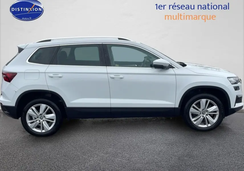 Vue latérale droite d'un Skoda Karoq blanc glacial avec jantes alu et barres de toit visibles.