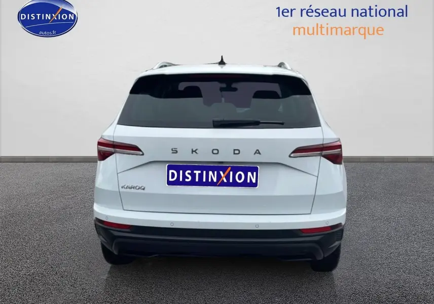 Vue arrière d'un SKODA KAROQ blanc glacial avec feux arrière LED et barres de toit visibles.