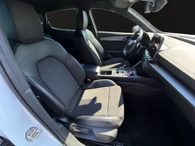 Vue intérieure côté conducteur de la CUPRA Formentor blanc 2025, sièges noirs, volant cuir, écran tactile central lumineux.