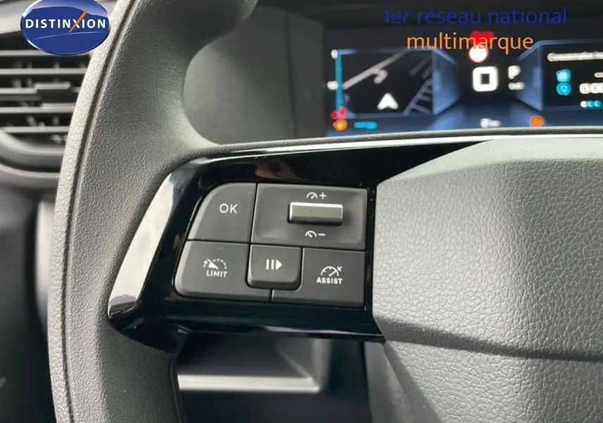 Gros plan sur les commandes au volant gauche du Citroën Jumpy gris Artense, avec écran numérique en arrière-plan.