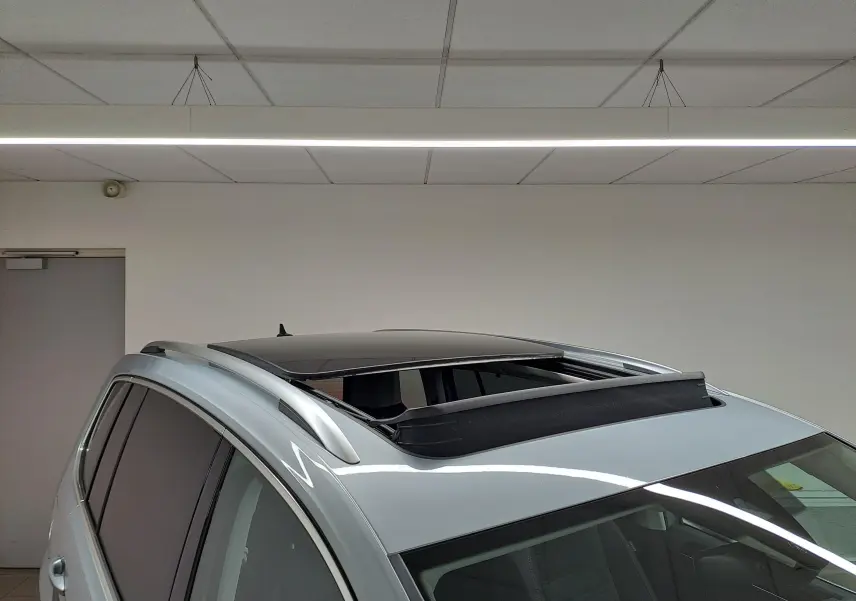 Vue en plongée du toit ouvrant panoramique ouvert d'un Volkswagen Touran gris argent, avec barres de toit visibles.