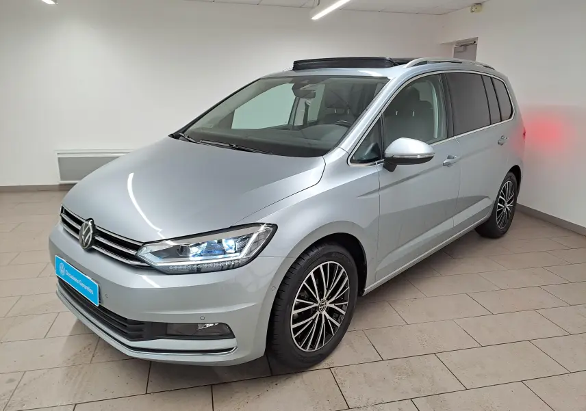 Volkswagen Touran gris argent en 3/4 avant droit, avec toit ouvrant panoramique et jantes alliage noires.