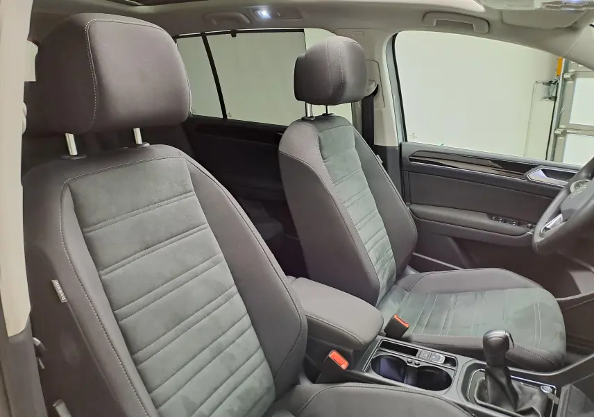 Vue intérieure côté droit du Volkswagen Touran 2025, sièges tissu gris et toit ouvrant panoramique visible.