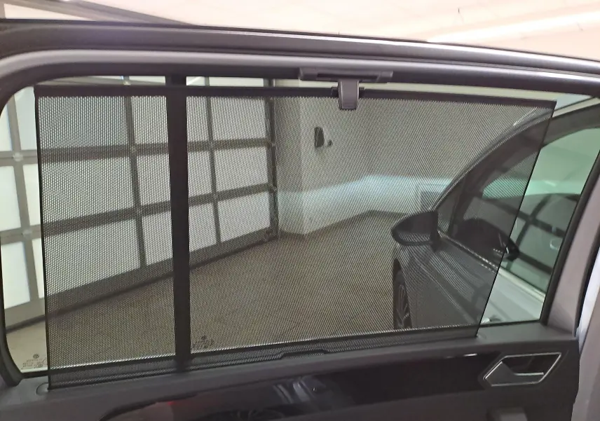 Vue intérieure côté gauche du Volkswagen Touran gris argent 2025, avec store pare-soleil manuel sur la vitre arrière.