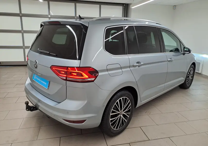 Vue 3/4 arrière droit d’un Volkswagen Touran gris argent avec hayon fermé et attelage escamotable visible en intérieur.