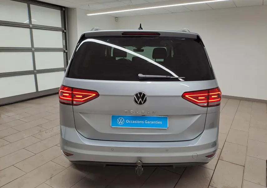 Vue arrière d'un Volkswagen Touran gris argent avec feux allumés et attelage visible dans un garage.