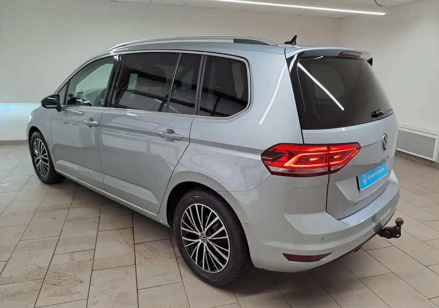 Vue 3/4 arrière droite du Volkswagen Touran gris argent avec toit ouvrant et attelage escamotable visible en intérieur showroom.