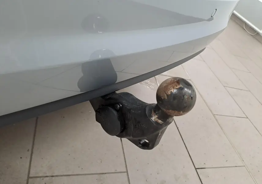 Gros plan sur le crochet d'attelage escamotable noir sous le pare-chocs arrière gris argent du Volkswagen Touran 2025.