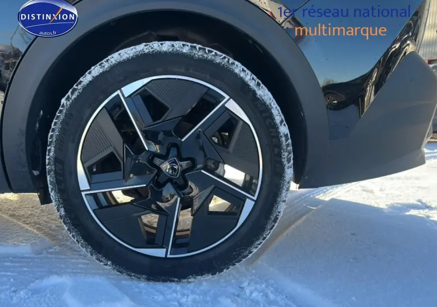 Gros plan sur la roue avant gauche noire d'une Peugeot 408 Hybrid 145 GT e-dcs6, jante alu design en hiver.