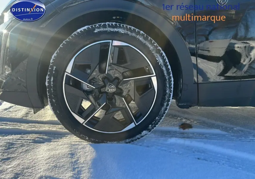 Gros plan sur la roue avant gauche d’une Peugeot 408 Hybrid 145 GT noire, avec jante alu et neige au sol.