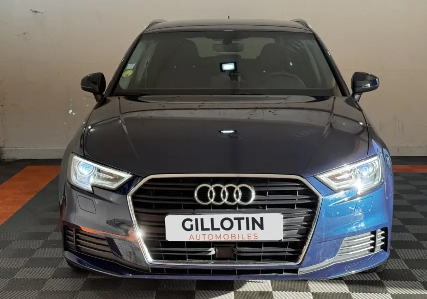 Vue avant d'une Audi A3 2.0 TDI 150 Business Line bleu métallisé avec phares allumés en intérieur.