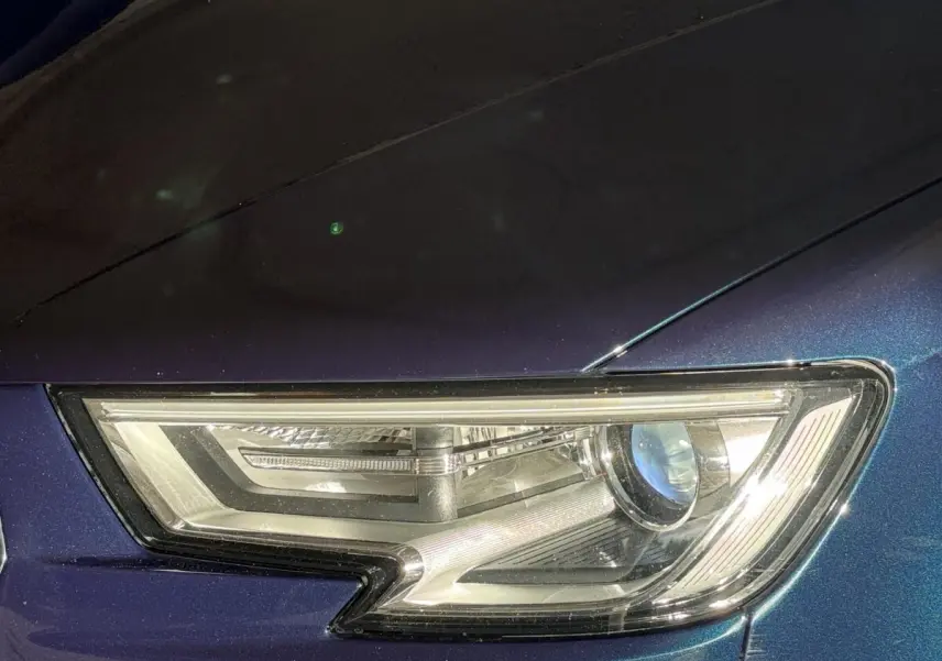 Gros plan sur le phare avant droit d’une Audi A3 bleu métallisé, mettant en valeur son design LED distinctif.