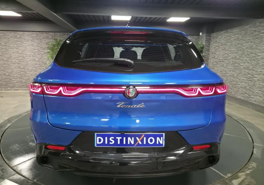 Vue arrière d'une Alfa Romeo Tonale bleu métallisé avec feux LED distinctifs et logo central dans un showroom.