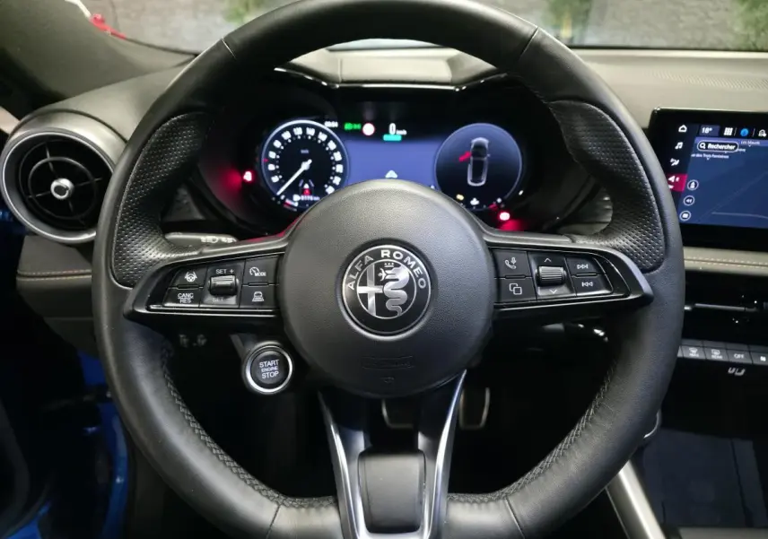 Vue rapprochée du volant cuir noir perforé de l'Alfa Romeo Tonale 2025 avec tableau de bord digital et bouton start/stop.