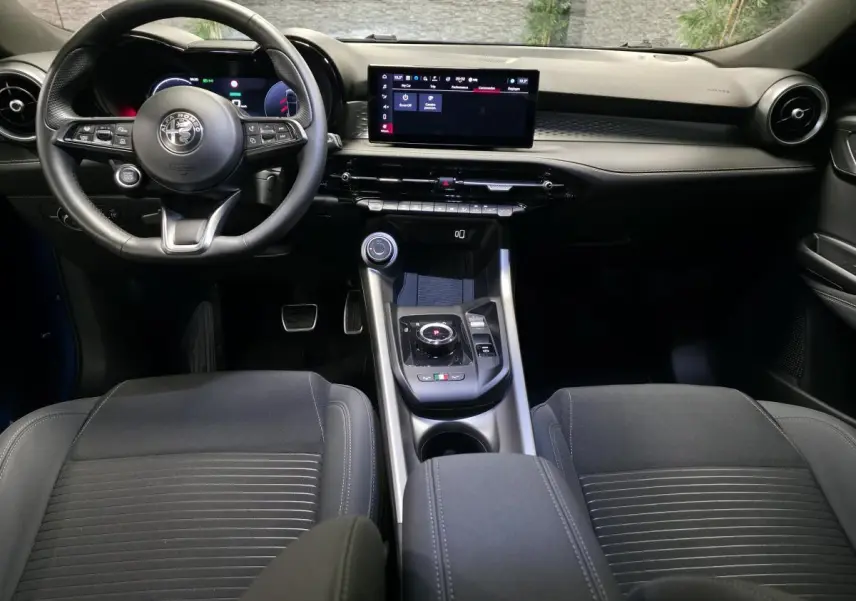 Vue intérieure avant de l'Alfa Romeo Tonale 2025, tableau de bord noir avec écran tactile et volant sport cuir.
