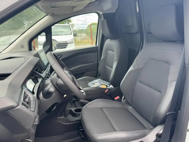 Vue intérieure côté conducteur du Renault Kangoo Van blanc, sièges tissu noir et tableau de bord moderne.