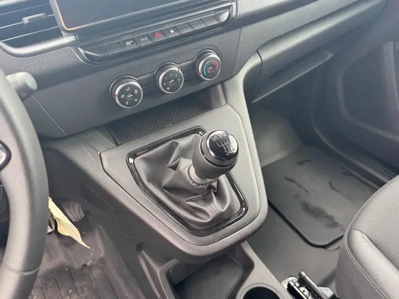 Vue intérieure côté conducteur du levier de vitesse manuel noir et des commandes de climatisation du Renault Kangoo blanc 2024.