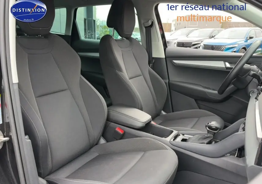 Intérieur avant du Skoda Karoq noir 2025, vue côté droit montrant sièges tissu gris et console centrale avec accoudoir.