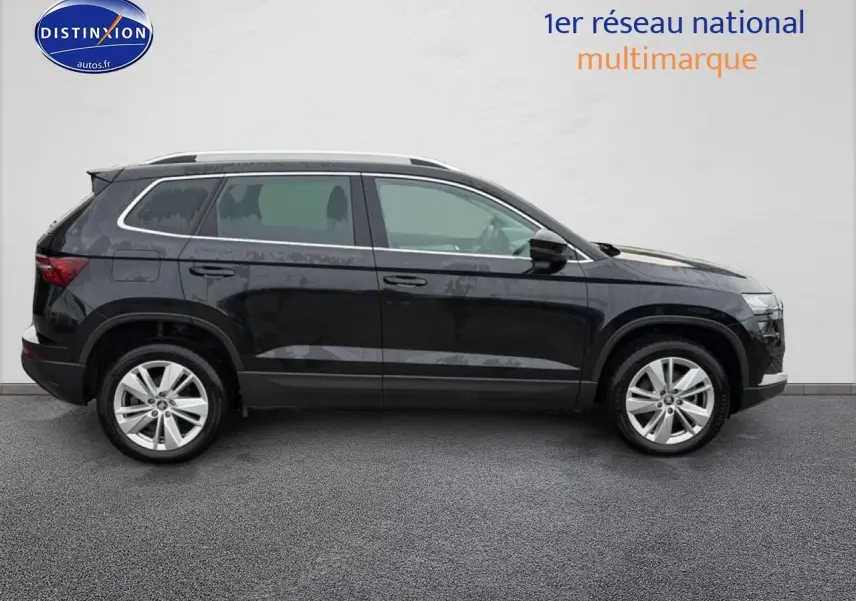 Profil droit d'un SUV Škoda Karoq noir 2025 avec jantes alu et barres de toit argentées sur fond neutre.