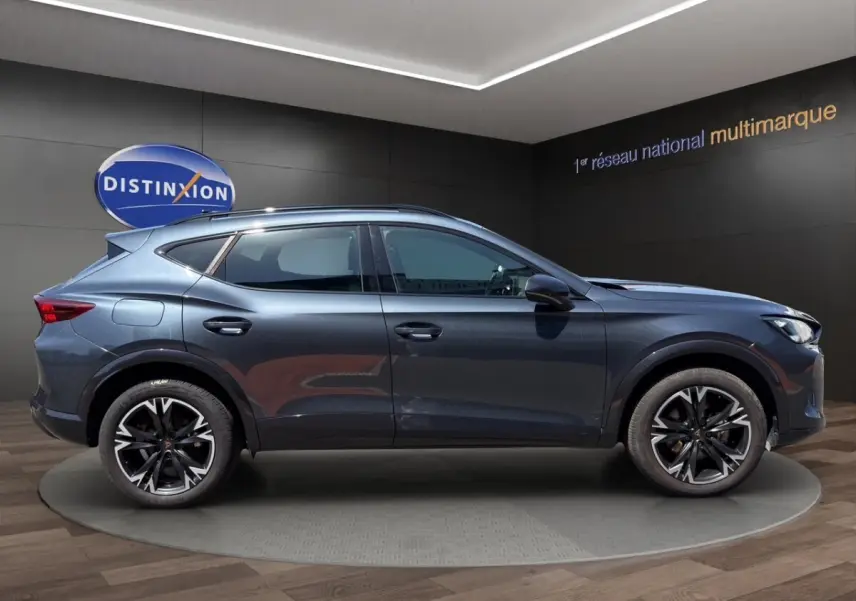 Profil droit du CUPRA Formentor gris foncé 2025 avec jantes alliage noires et toit ouvrant visible en intérieur showroom.