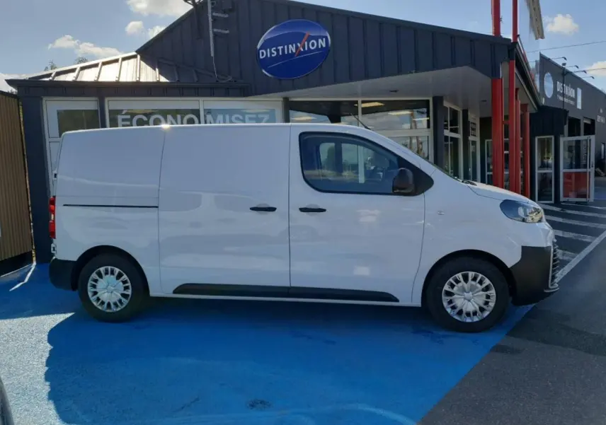 Vue de profil côté droit du Toyota Proace Fourgon blanc Glacier garé devant un bâtiment commercial.
