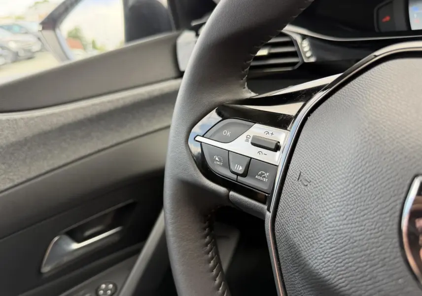 Gros plan sur le volant noir avec commandes intégrées côté gauche et partie de la porte intérieure grise d’une Peugeot 308 SW rouge.
