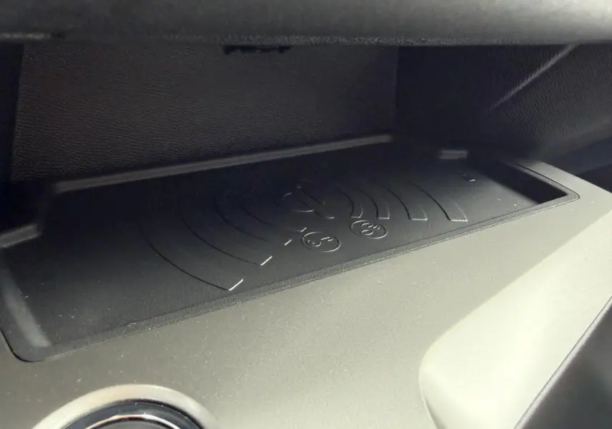 Gros plan sur le chargeur sans fil noir intégré dans l'habitacle de la Peugeot 308 SW 1.6 PHEV rouge, année 2024.