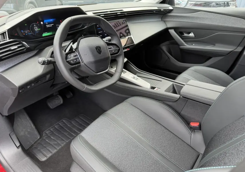Intérieur avant droit de la Peugeot 308 SW 2024, avec tableau de bord numérique et sellerie tissu gris à surpiqûres bleues.