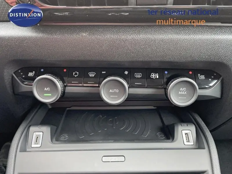 Gros plan sur la console centrale noire de la Citroën C4 2024 montrant les commandes de climatisation automatique et chargeur sans fil.