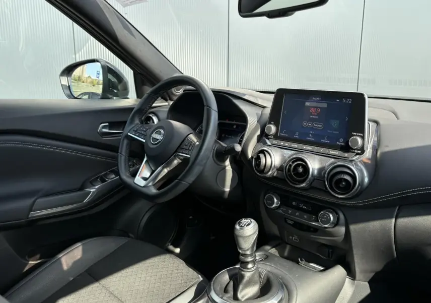 Intérieur du Nissan Juke 2024 vu côté conducteur, volant multifonction, écran tactile et levier de vitesse manuel visibles.