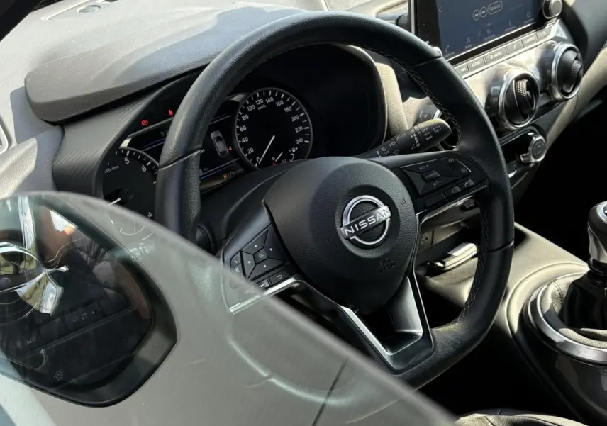 Vue rapprochée du volant noir et du tableau de bord du Nissan Juke 2024, avec levier de vitesses manuel visible.