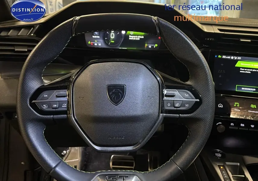 Vue rapprochée du volant cuir noir avec logo Peugeot et commandes intégrées, tableau de bord digital en arrière-plan.