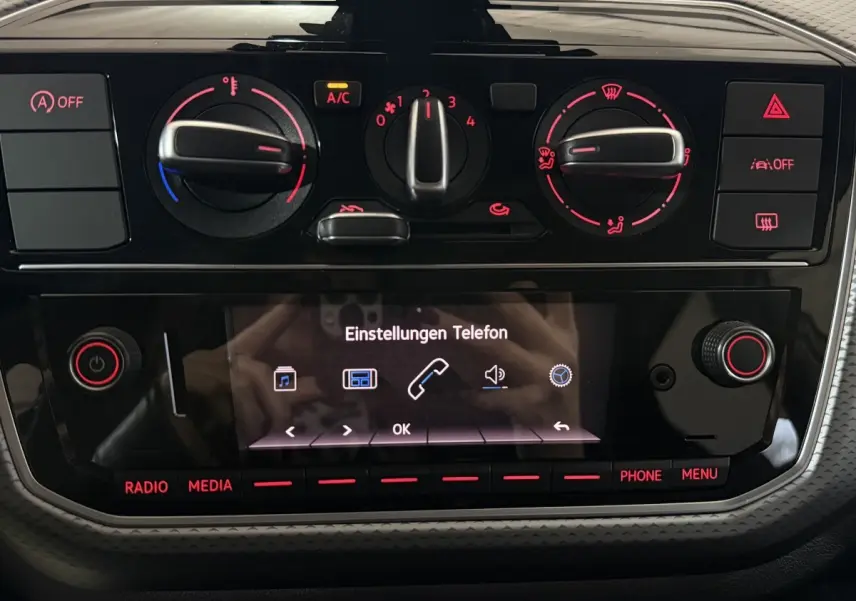 Tableau de bord noir du Volkswagen Up 2022 avec commandes de climatisation et écran tactile central allumé.