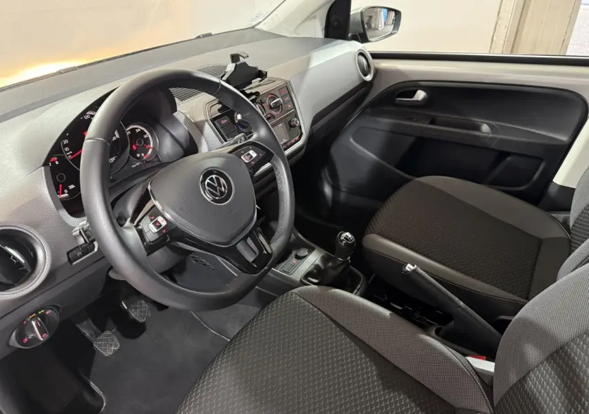 Vue intérieure côté conducteur de la Volkswagen Up 1.0 65 Active 2022, volant cuir et sièges tissu gris foncé.