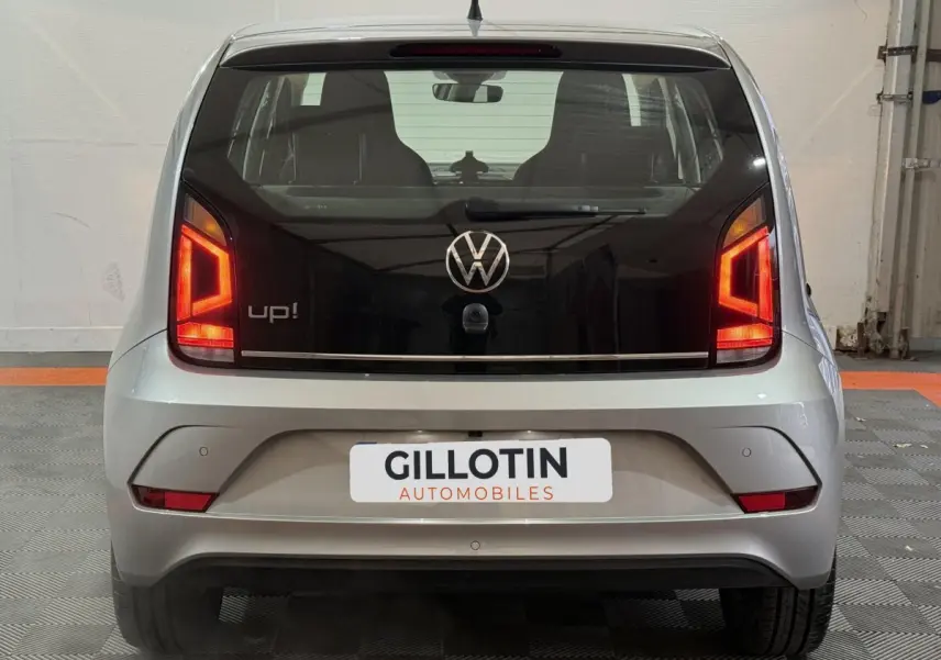 Vue arrière d'une Volkswagen Up! gris foncé avec feux arrière allumés et logo VW visible sur le hayon noir.