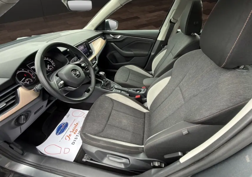 Vue intérieure côté conducteur du Skoda Kamiq 2023 gris foncé, mettant en valeur les sièges tissu bicolores et le tableau de bord avec écran tactile.