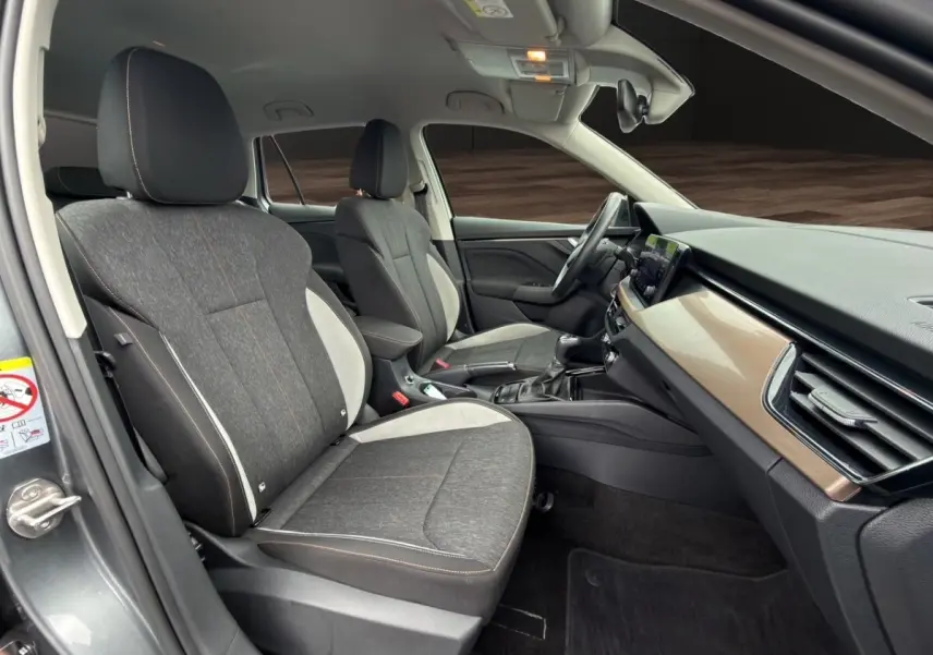 Vue intérieure côté conducteur du Skoda Kamiq 2023, sièges tissu gris bicolore avec tableau de bord bois clair.