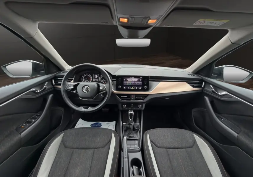Vue intérieure avant du Skoda Kamiq 2023 gris foncé, avec tableau de bord clair et écran tactile central.