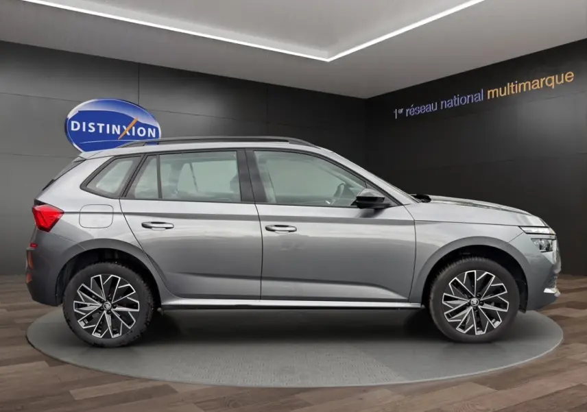 Vue de profil côté gauche du Skoda Kamiq gris foncé 2023 avec jantes bi-ton et barres de toit noires.