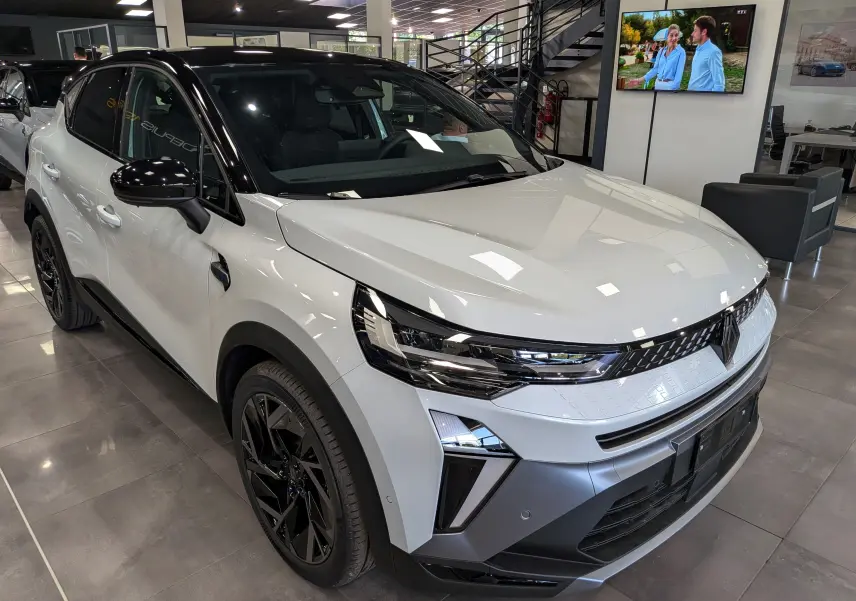 Renault Captur E-Tech hybride blanc nacré avec toit noir, vue 3/4 avant droit en intérieur showroom.