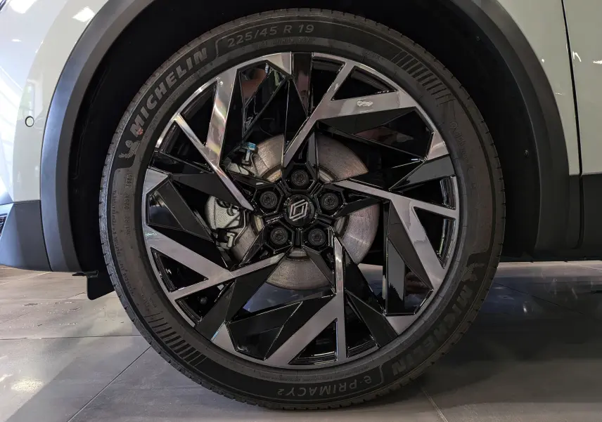Gros plan sur la roue avant gauche du Renault Captur blanc nacré, jante alliage noire et argentée au design géométrique.