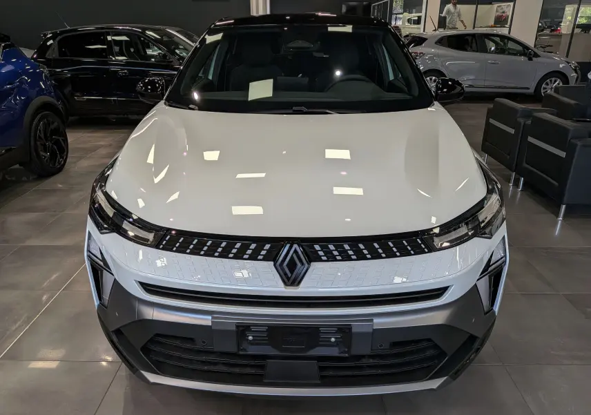 Vue avant d'un Renault Captur E-TECH blanc nacré avec toit noir, mettant en valeur la calandre lumineuse et le logo central.