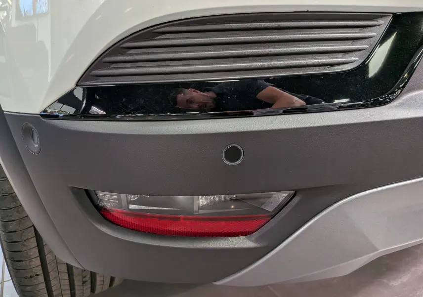Gros plan sur le pare-chocs avant droit blanc nacré du Renault Captur E-TECH avec feux antibrouillard et capteurs de stationnement.