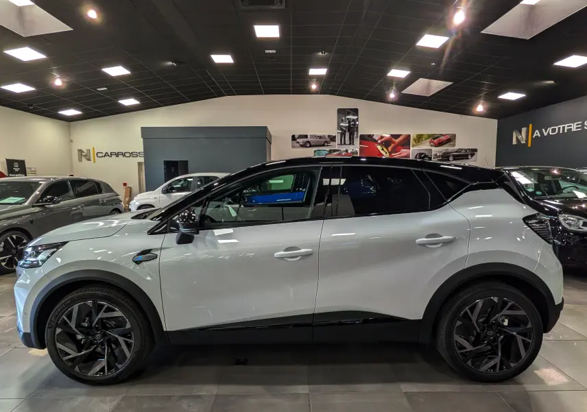 Profil côté gauche du Renault Captur E-TECH 160 ch blanc nacré avec toit noir et jantes noires en concession.