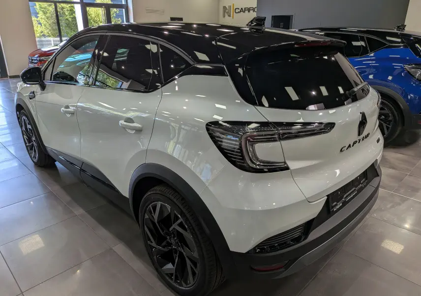 Renault Captur E-Tech blanc nacré avec toit noir, vue 3/4 arrière droit en intérieur showroom.