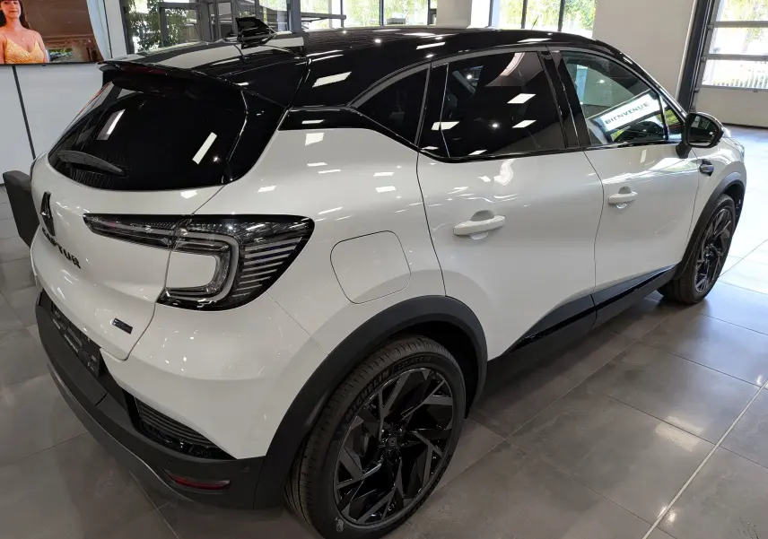 Vue 3/4 arrière droite du Renault Captur E-TECH blanc nacré avec toit noir et jantes noires en showroom.