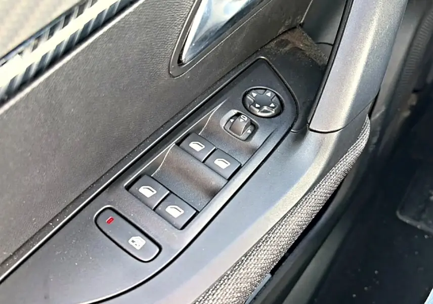 Gros plan sur la commande des vitres électriques côté gauche, avec tissu gris et plastique noir dans l’habitacle Peugeot 2008.