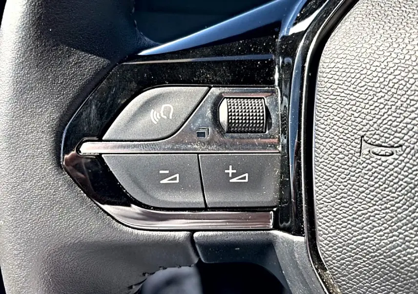 Gros plan sur les commandes de volume et appel mains-libres du volant noir du Peugeot 2008 gris 2025.